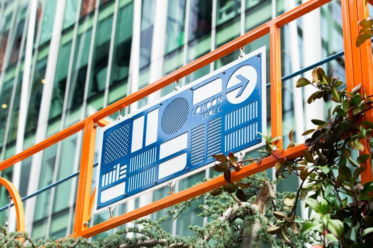 A sign for the Moor Lane Community Garden, it is blue and white, with orange steel around it
